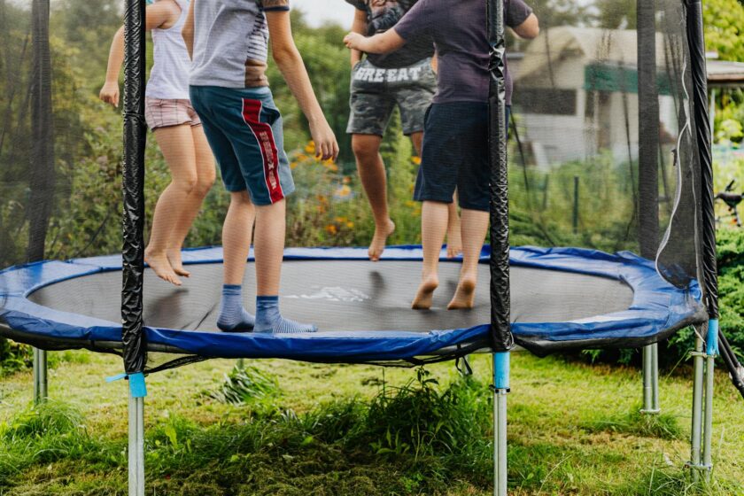 Group of kids jumping and playing on an outdoor trampoline in a backyard.